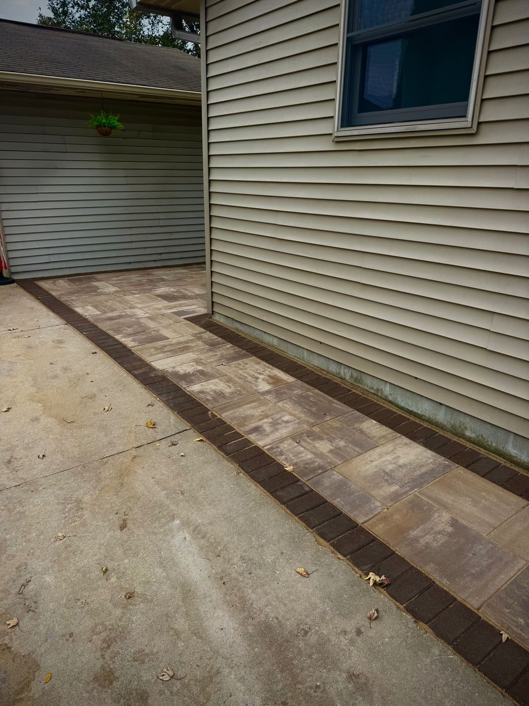 Narrow paver pad along the side of a home with a dark soldier-course border